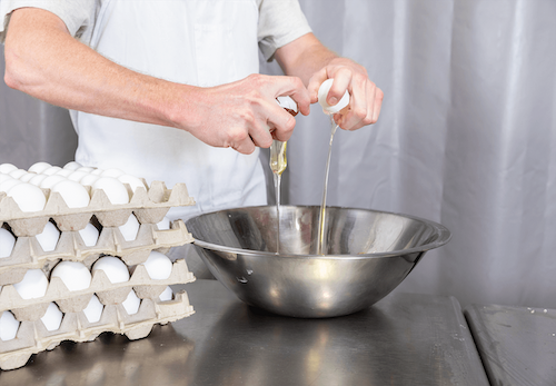A chef cracking eggs into a metal bowl